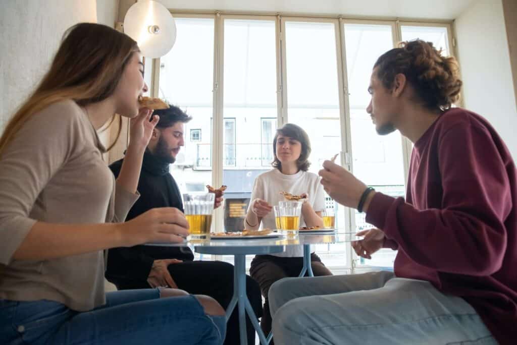 Four young people eating pizza and drinking beer at a restaurant