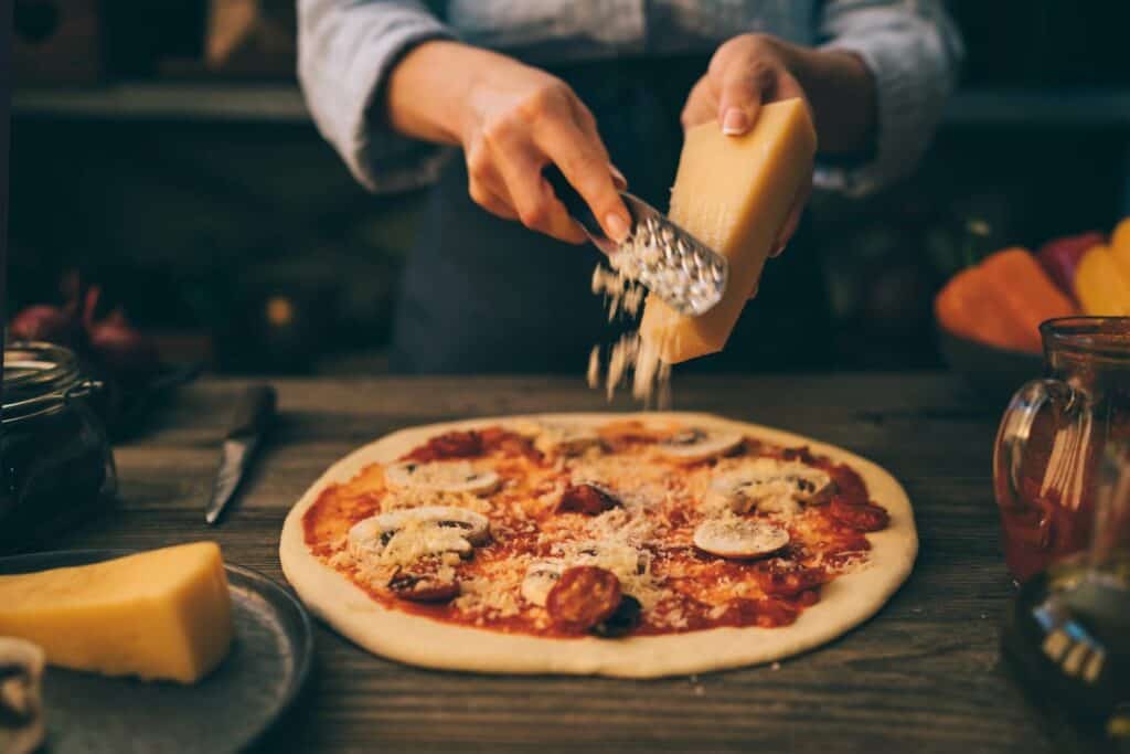 A woman grate cheese on pizza