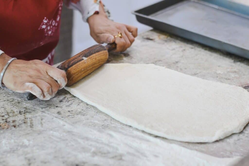 A woman off-screen rolling pizza dough