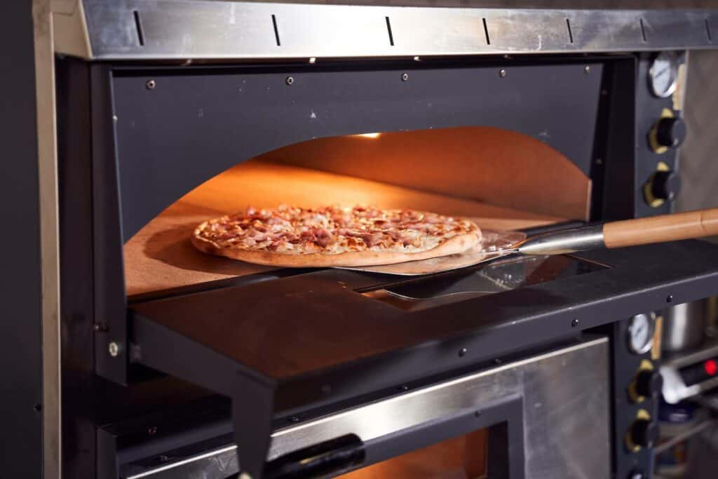 A person placing the pizza in an oven