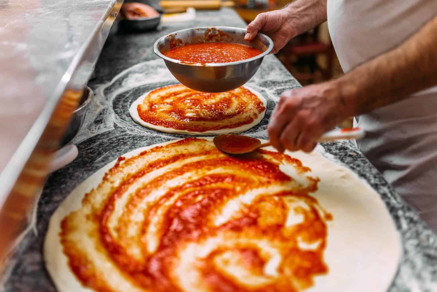 A pizza chef putting tomato sauce on pizza dough