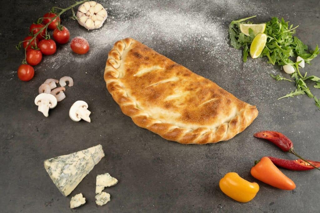 Baked calzone with ingredients around it