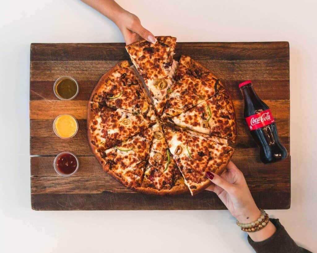 Pizza on a wooden board next to dipping sauces