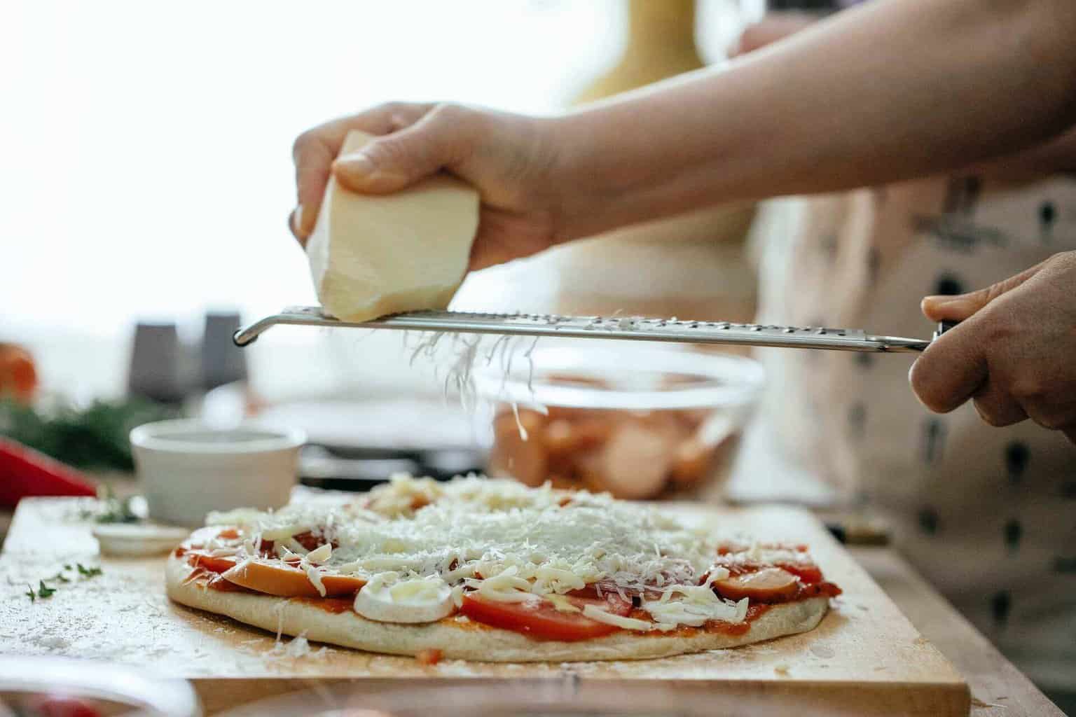 Person grating cheese on a pizza