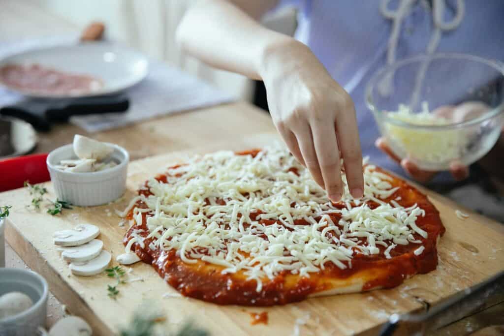 Person putting cheese on a pizza
