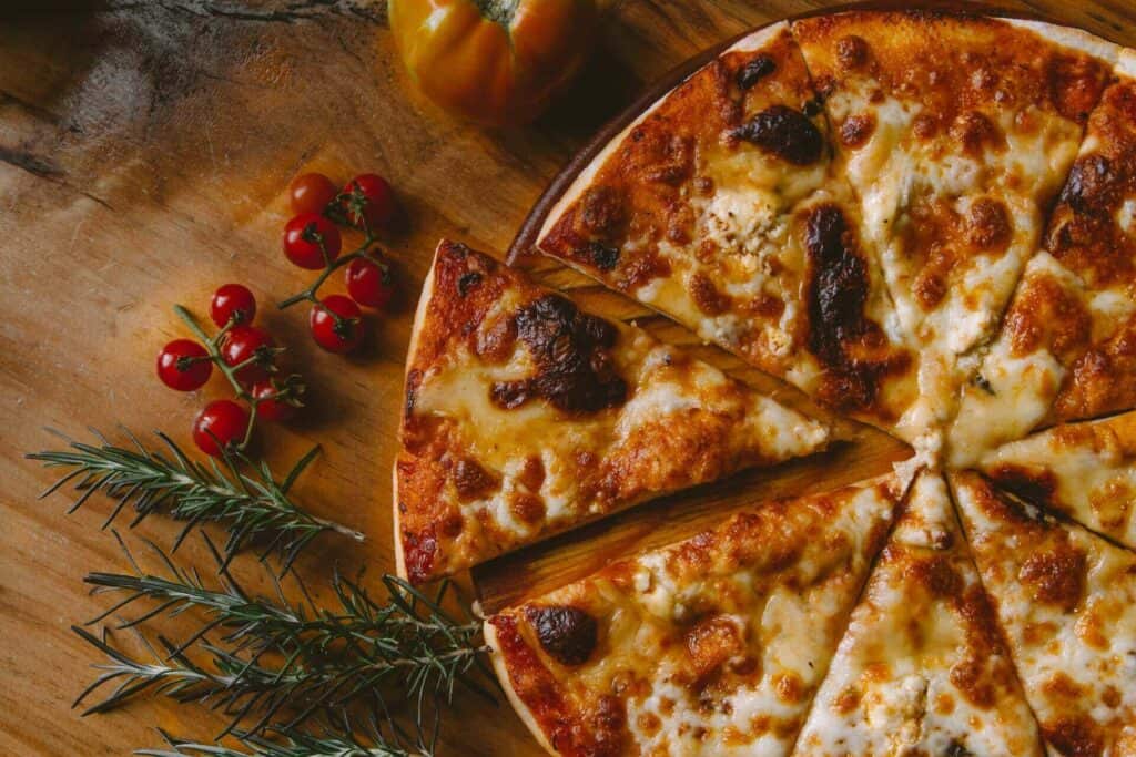 A cheese pizza and tomatoes and rosemary next to it 