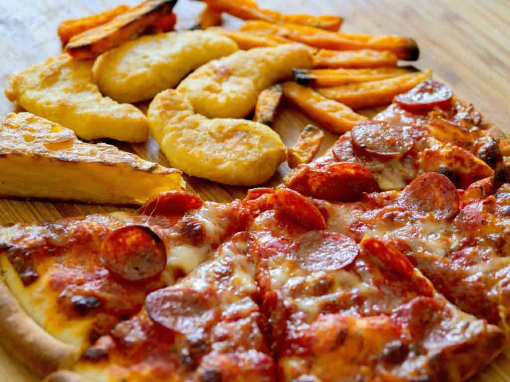 Pizza slices next to chicken wings and fries