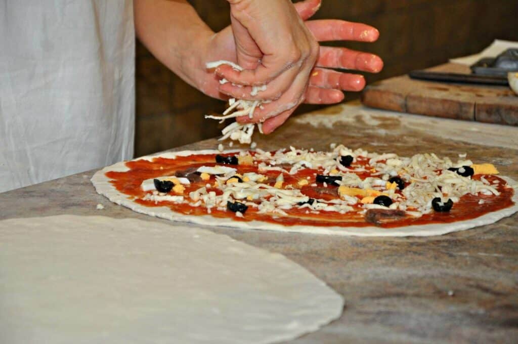 Person adding toppings on a pizza