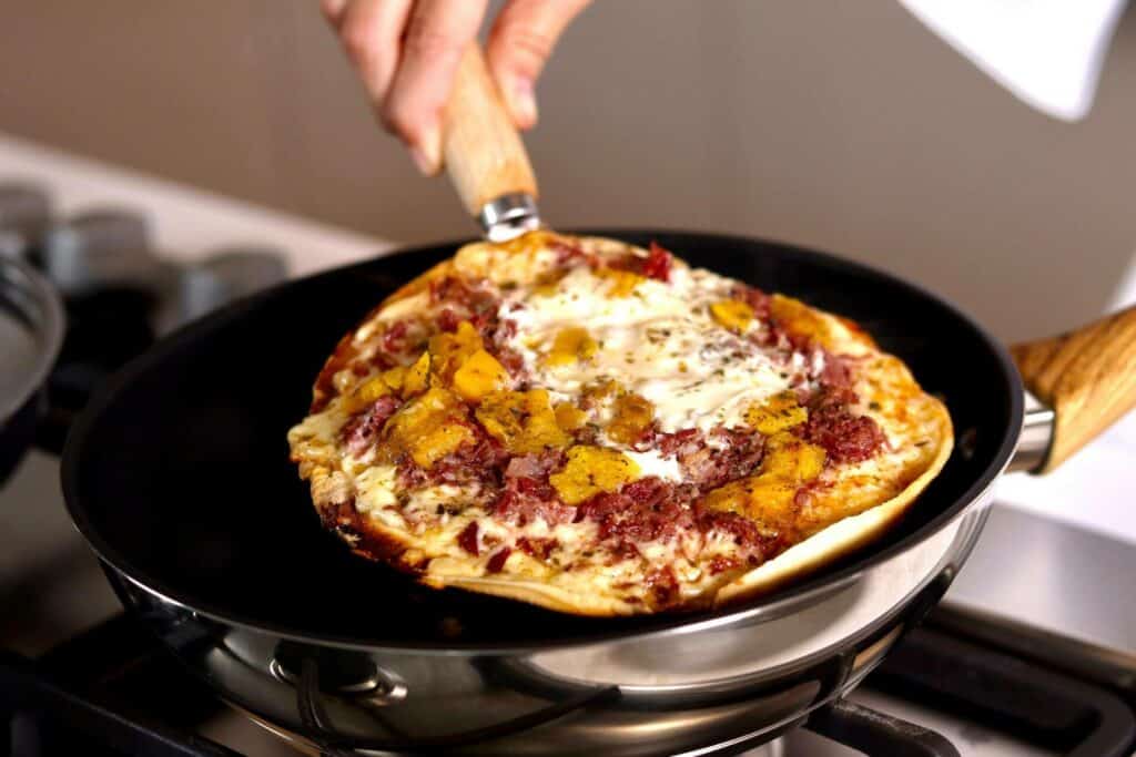 Person cooking a pizza on a frying pan