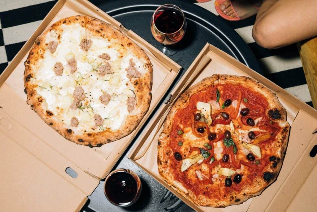 Two different pizzas next to wine glasses