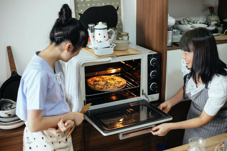 Two women looking at a pizza in the oven